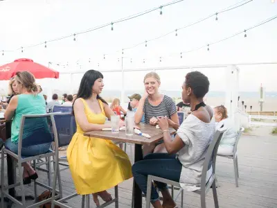Three people sitting outdoors on a restaurant deck restaurant at the beach.