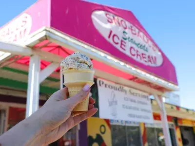 An ice cream cone being held up in front of a ice cream shop.